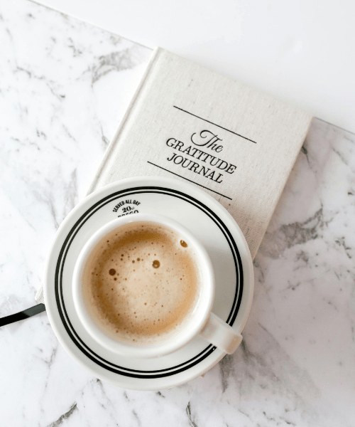 Cup of coffee on a gratitude journal, symbolizing the power and impact of good habits as a creative solopreneur on work and personal life.