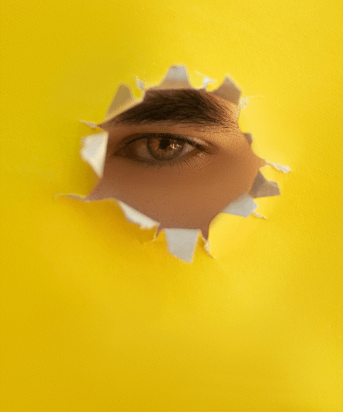 A woman's eye looking through a poked hole in a piece of paper, symbolizing overcoming creative block as an Artist or Designer.