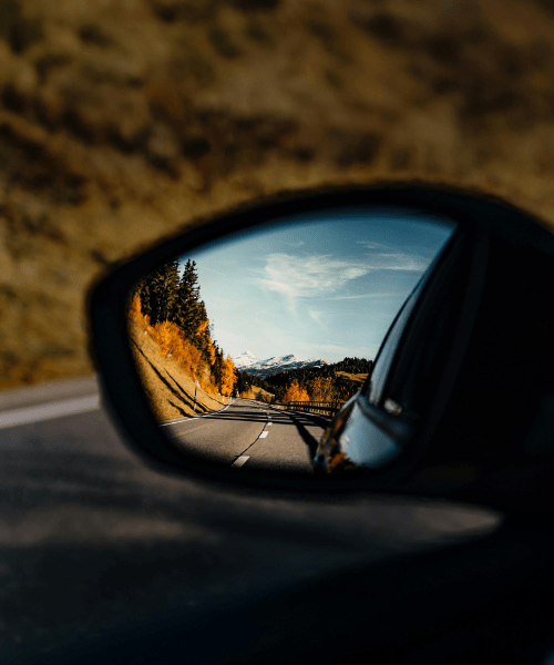 Rear view mirror of a car with a beautiful landscape, symbolizing celebrating wins for creative entrepreneurs doing their yearly review and reflection.