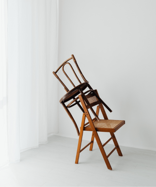 Two wooden chairs in a bright minimal room, one balancing on the other, symbolizing work-life balance for Artists and Designers.